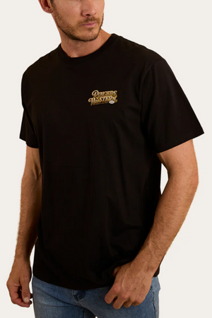 A man stands against a plain, light background wearing blue jeans and a black Ringers Western Cowboys Can Dance Loose Fit T-Shirt with a small gold and white "Records Western Co." logo on the left chest.