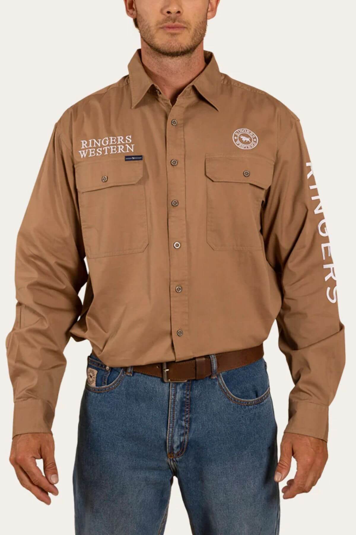 A man wearing a Ringers Western Hawkeye Embroidered Shirt in brown, featuring "Ringers Western" embroidered on the left chest pocket and sleeve. Made of premium cotton for comfort and offering UPF 50+ sun protection, the shirt includes two chest pockets with flaps. He pairs it with blue jeans and a brown belt against a plain white background.