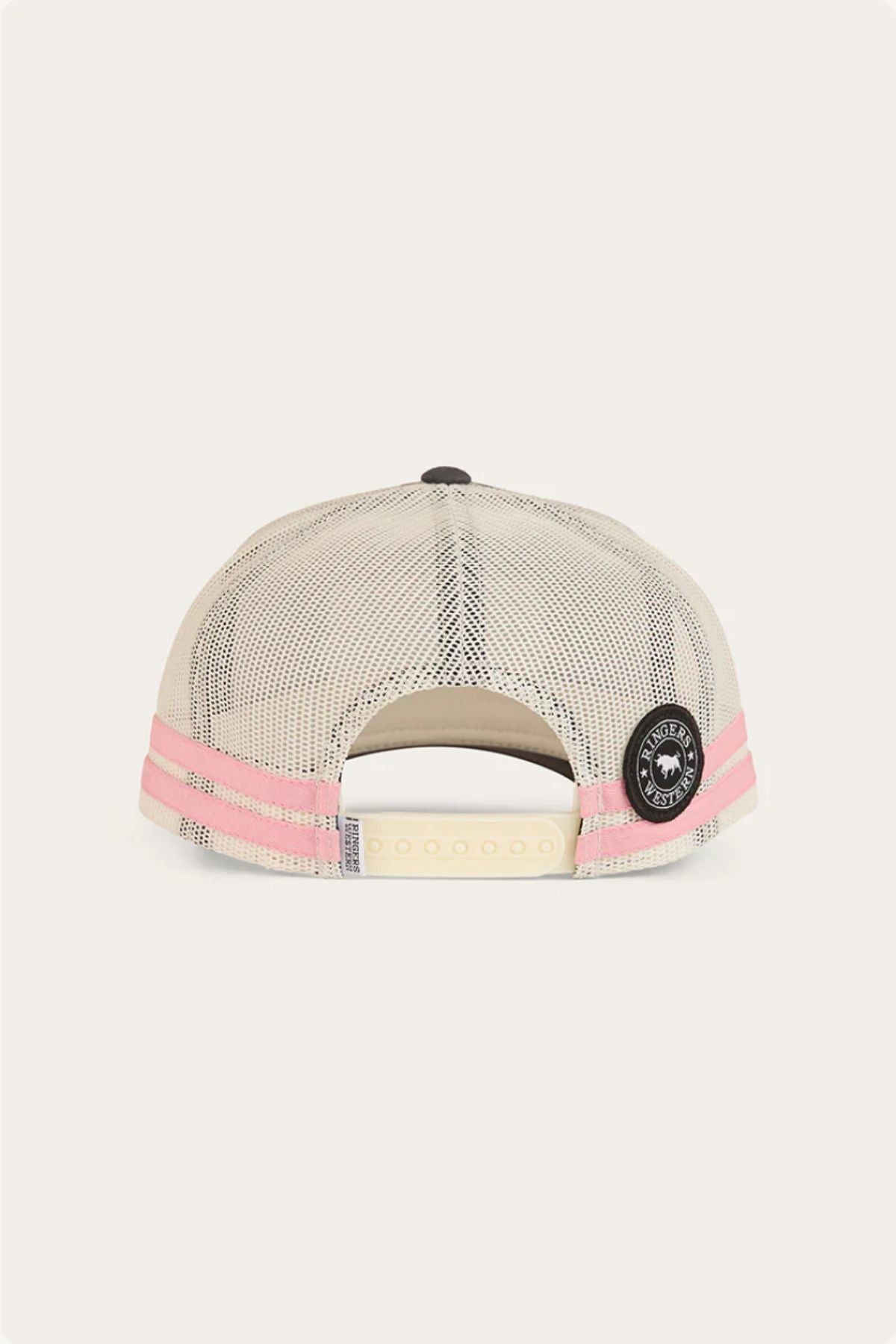 The Ringers Western Hometown Trucker Cap is shown from behind, with light beige mesh, pink stripes, an adjustable snapback closure, and a round black patch on the right side.