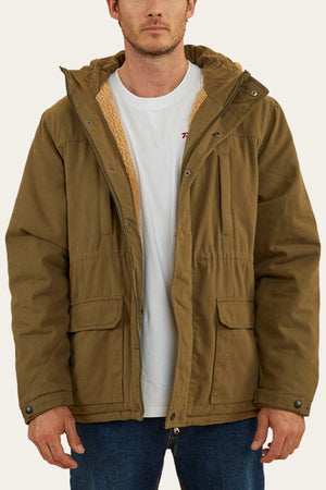 A man wearing a khaki Ringers Western Judd Jacket over a white t-shirt and blue jeans. The jacket, featuring large front pockets and a sherpa lining visible around the collar, has a removable hood. The man is standing facing the camera with his hands relaxed at his sides.