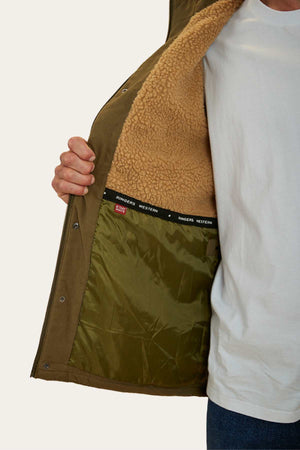 A person wears an open Ringers Western Judd Jacket with a brown sherpa lining, showing the inner part of the jacket and the "RINGERS WESTERN" label. The person is also wearing a white T-shirt and jeans.
