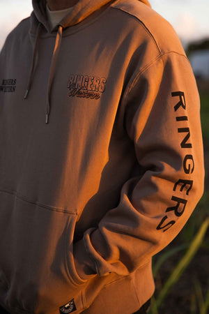 A person stands outdoors in warm sunlight wearing the Ringers Western KNX Oversized Hoodie, featuring cozy brushed fleece, "Ringers Western" across the chest, and bold "Ringers" lettering along the sleeve.