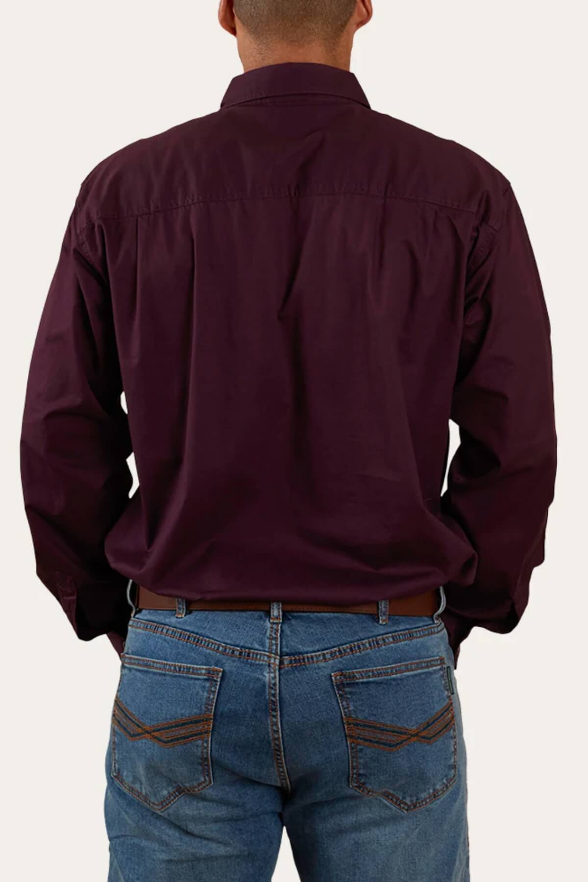 A person is pictured from behind wearing the Ringers Western King River Half Button Shirt in a dark maroon color and blue jeans. The image focuses on the upper back and rear view, highlighting the details of the comfortable, hard-wearing work shirt and jeans against a plain background.