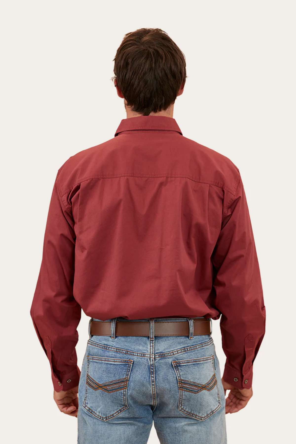 A person with short dark hair is shown from the back, wearing a long-sleeved Ringers Western King River Half Button Shirt tucked into blue jeans. The individual is standing against a plain light background.