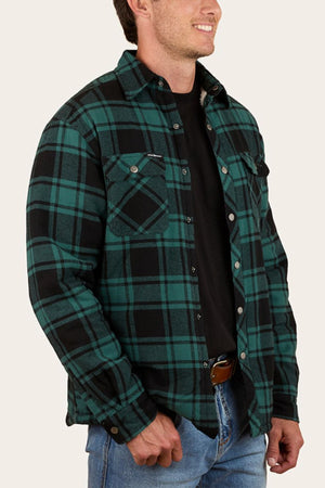 A man wearing the Ringers Western Sawyer Flannel Shirt over a black t-shirt and blue jeans stands with one hand in his pocket, facing slightly to the side and smiling.