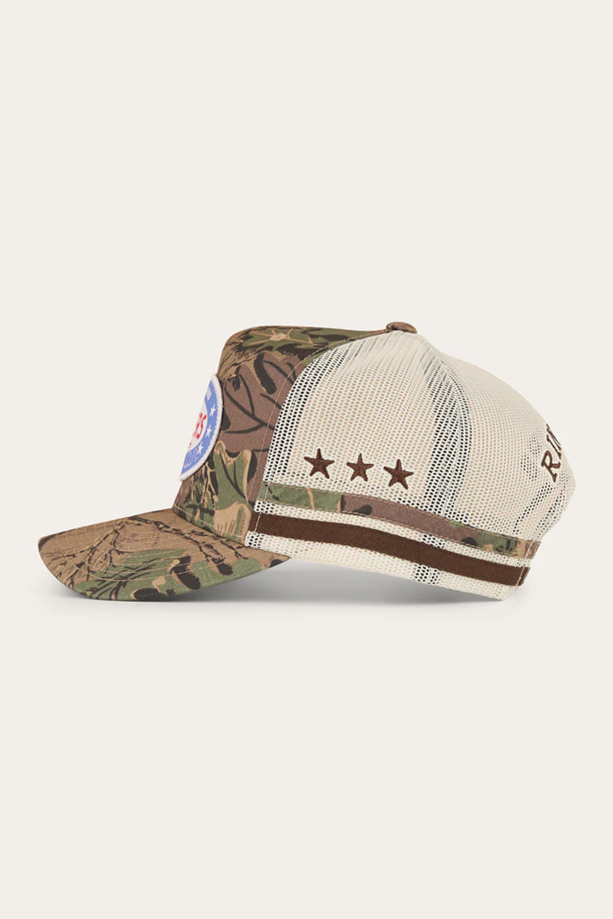 The Ringers Western Shooter Deep Fit Trucker Cap features a camouflage front, beige mesh back, brown star side detail, circular blue/red front patch, brown text on the mesh, and an adjustable snapback for a perfect fit.
