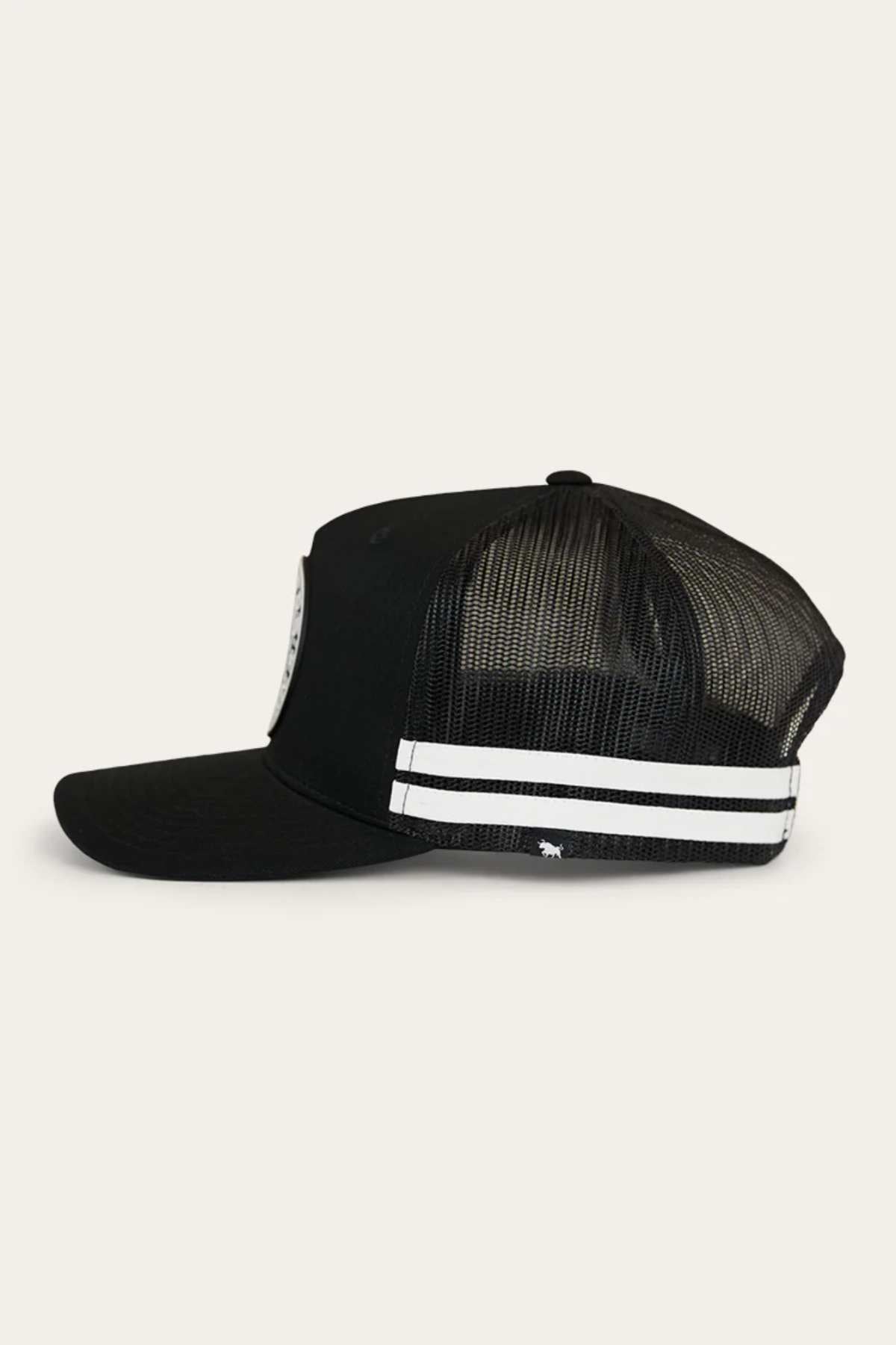 A side view of the Ringers Western Signature Bull Flag Trucker Cap, showcasing its black mesh design and curved brim. The cap features two white horizontal stripes on the side panel and a small logo near the base. Partially visible on the front panel is a circular patch. For an adjustable fit, this stylish hat comes equipped with a snapback closure.