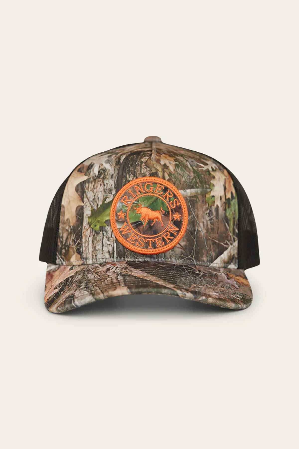 The Ringers Western Signature Bull Trucker Cap is a camouflage hat with an orange patch featuring a horse and the "Ringers Western" logo on the front. Made from cotton twill, it includes a mesh back and a curved brim.