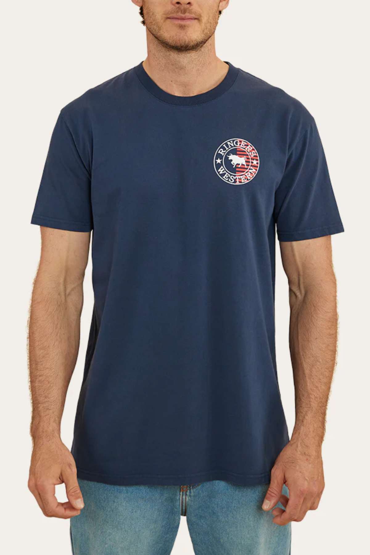 A man wearing a navy blue Ringers Western Signature Flag Stock Fit T-shirt, made from 100% cotton, featuring a circular logo on the left chest area with a red, white, and blue design and the text "Ranger USA Nest Fest." He has light skin and short, dark hair, and is also wearing light blue jeans.