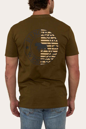 A man is wearing a Ringers Western Signature Flag Stock Fit T-Shirt in brown, crafted from soft cotton jersey. The back of the shirt features a large circular graphic that includes a stylized buffalo, stars, and surrounding text. He pairs it with blue jeans and has a small tattoo on his left arm.