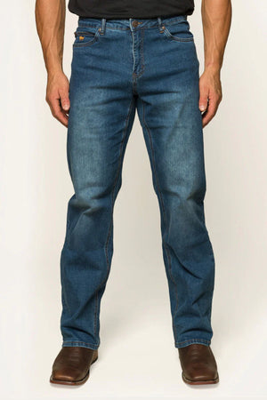 A man in Ringers Western Sturt Mens Relaxed Leg Jeans and brown boots stands against a neutral backdrop. The jeans, crafted from premium stretch denim, have a classic cut with visible stitching and slight fading on the thighs and knees. The lower part of a dark shirt is visible.