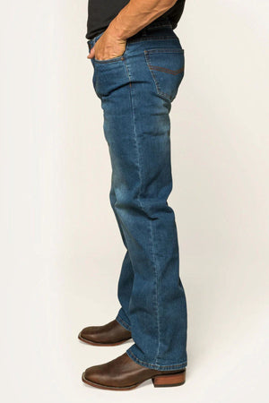 A person in Ringers Western Sturt Mens Relaxed Leg Jean stands sideways with one hand in the pocket. The jeans feature a relaxed fit, premium stretch denim, and a visible stitching pattern against a plain, light-colored background.