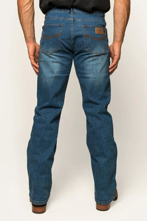 A rear view shows a person wearing Ringers Western Sturt Mens Relaxed Leg Jeans in blue with dark brown pocket stitching and a leather waistband patch, paired with a black shirt. The premium stretch denim stands out against the light-colored background.