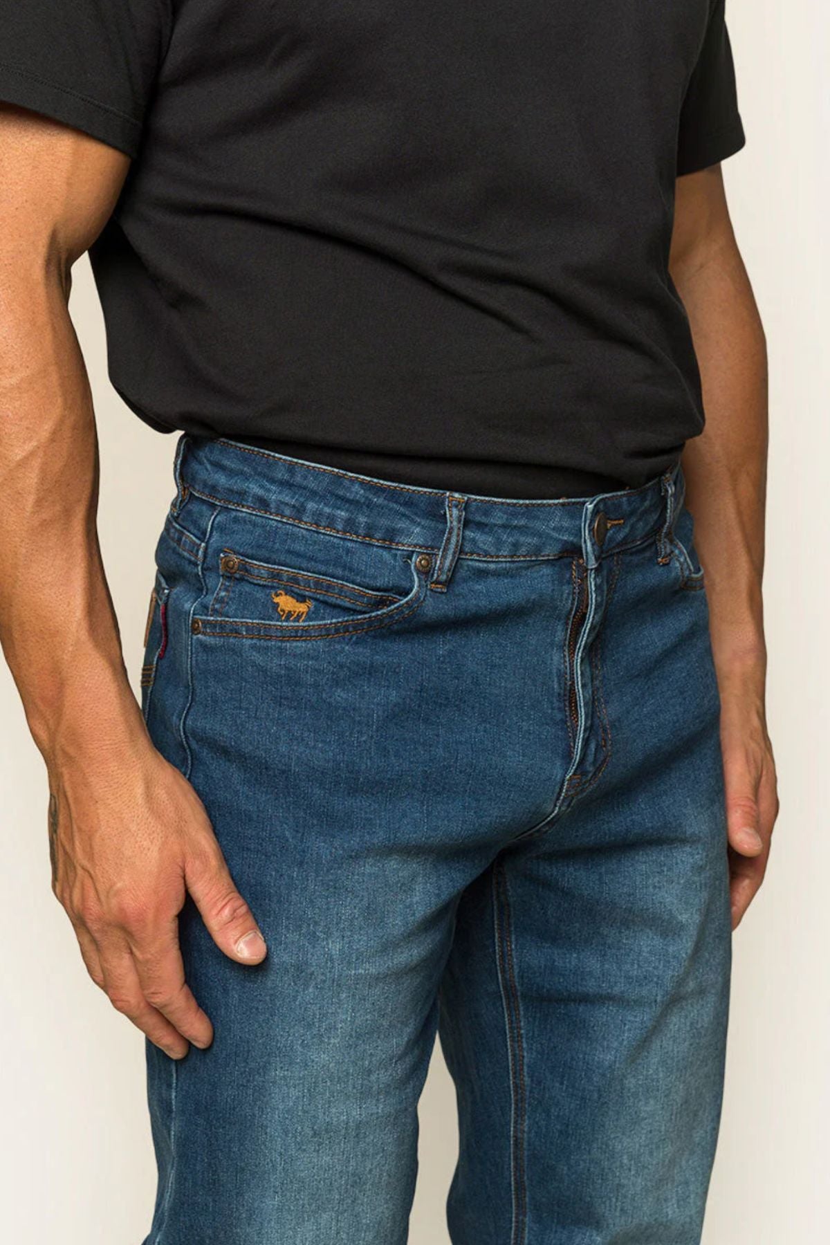 A person wears a black T-shirt with Ringers Western Sturt Men's Relaxed Leg Jeans, thumb hooked in the pocket. The jeans have a small brown label on one pocket, with only the torso and legs visible.