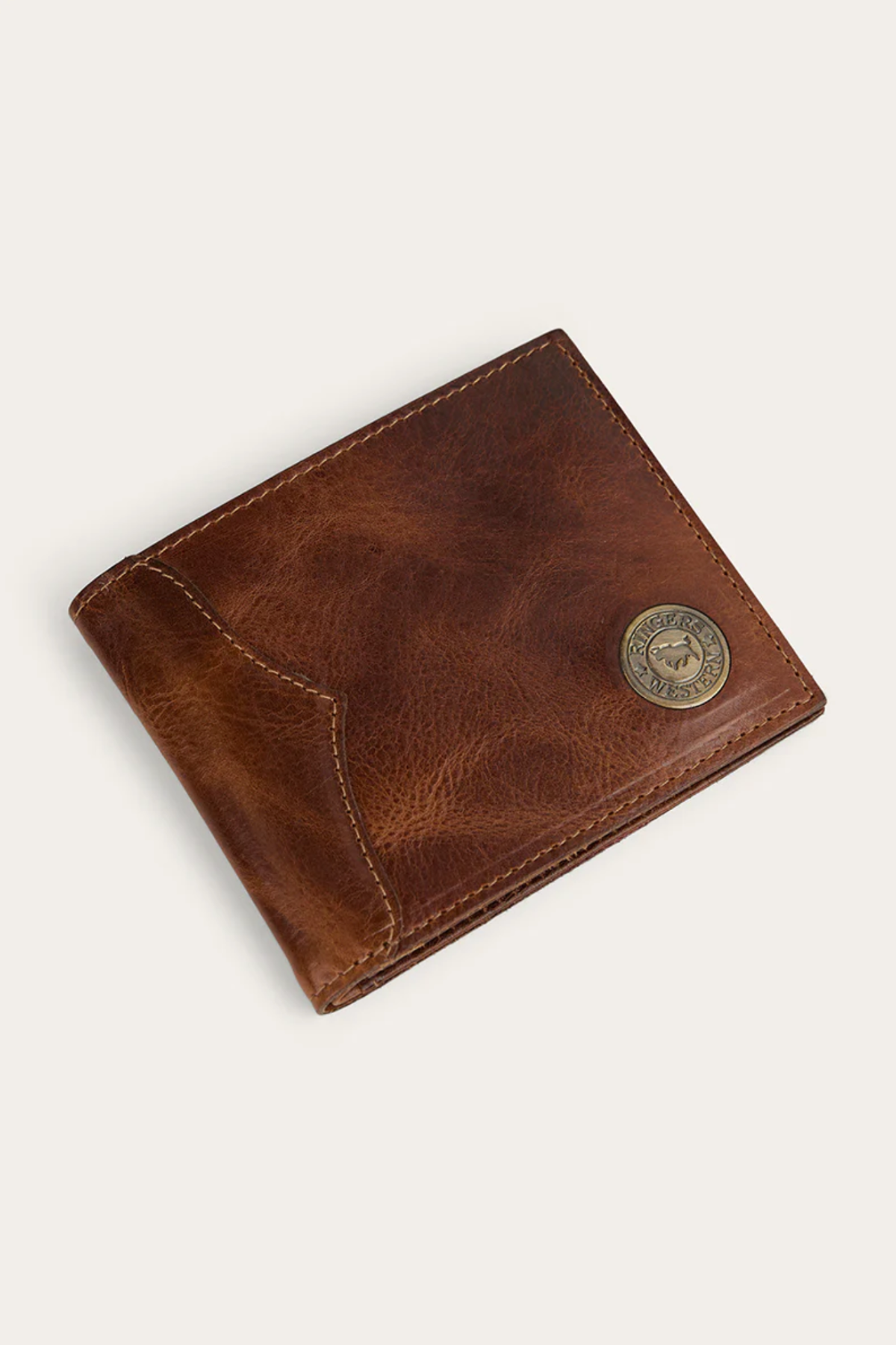 The Ringers Western Toro Midi Wallet is a slim brown full-grain leather wallet with visible stitching and a round metallic emblem in the bottom right, displayed on a plain light background.
