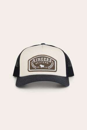 The Ringers Western Wheatbelt Trucker Cap features a white front, black mesh back, dark bill, and a brown patch with "RINGERS WESTERN 2012," a bull graphic, and laurel branches for a classic look.