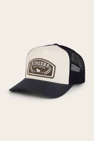 The Ringers Western Wheatbelt Trucker Cap is black and white with a breathable mesh back and a brown front patch featuring "Ringers Western," leaf designs, and a small cow silhouette.