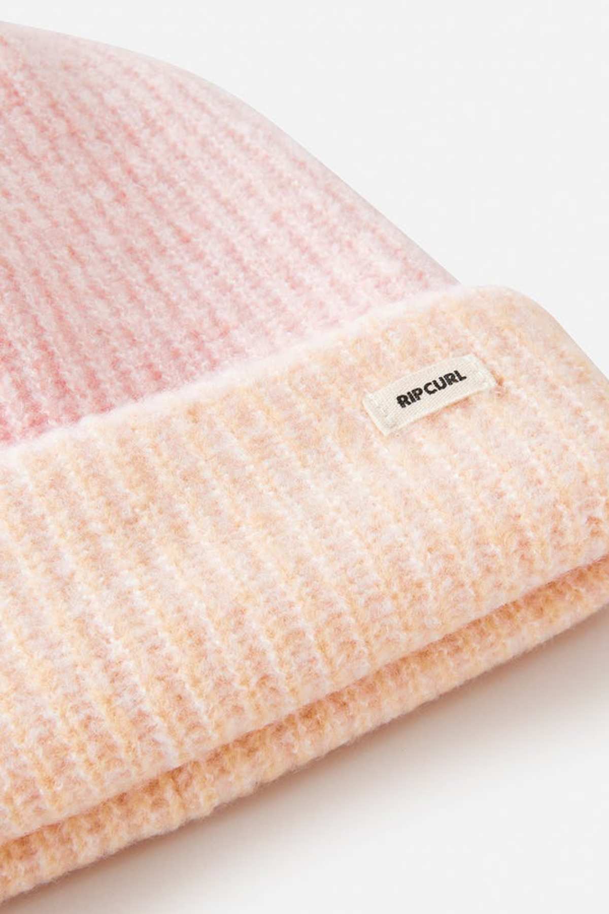 Close-up of a pink and peach Rip Curl 2 Tone Reg Revo Beanie with a small white "Rip Curl" label. This tall, ribbed beanie features a folded brim, ideal for adding style to any cold-weather outfit.