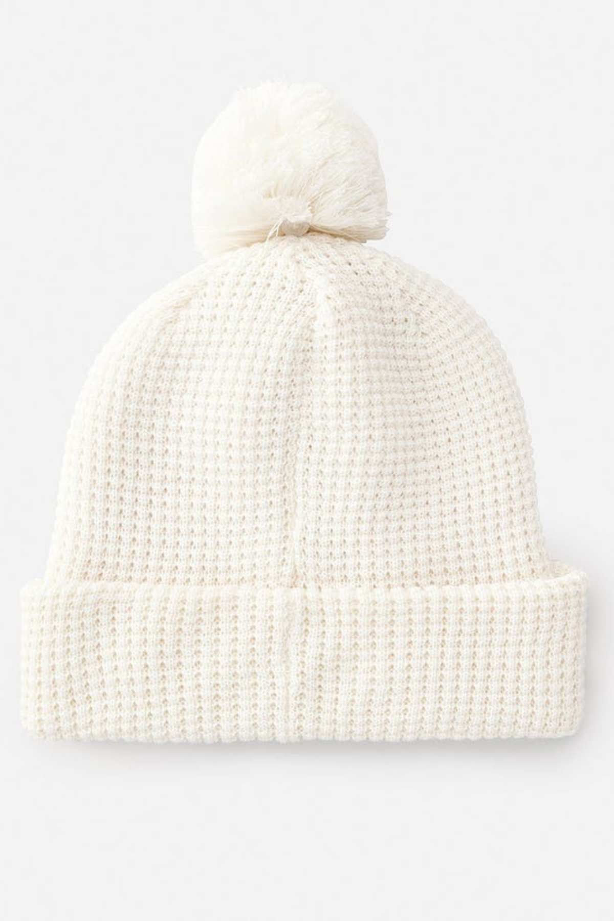 The Rip Curl Anoeta Reg Pom Pom Beanie showcases a white knit design with a folded brim, large pom-pom, and soft teddy fur lining, presented on a plain background.