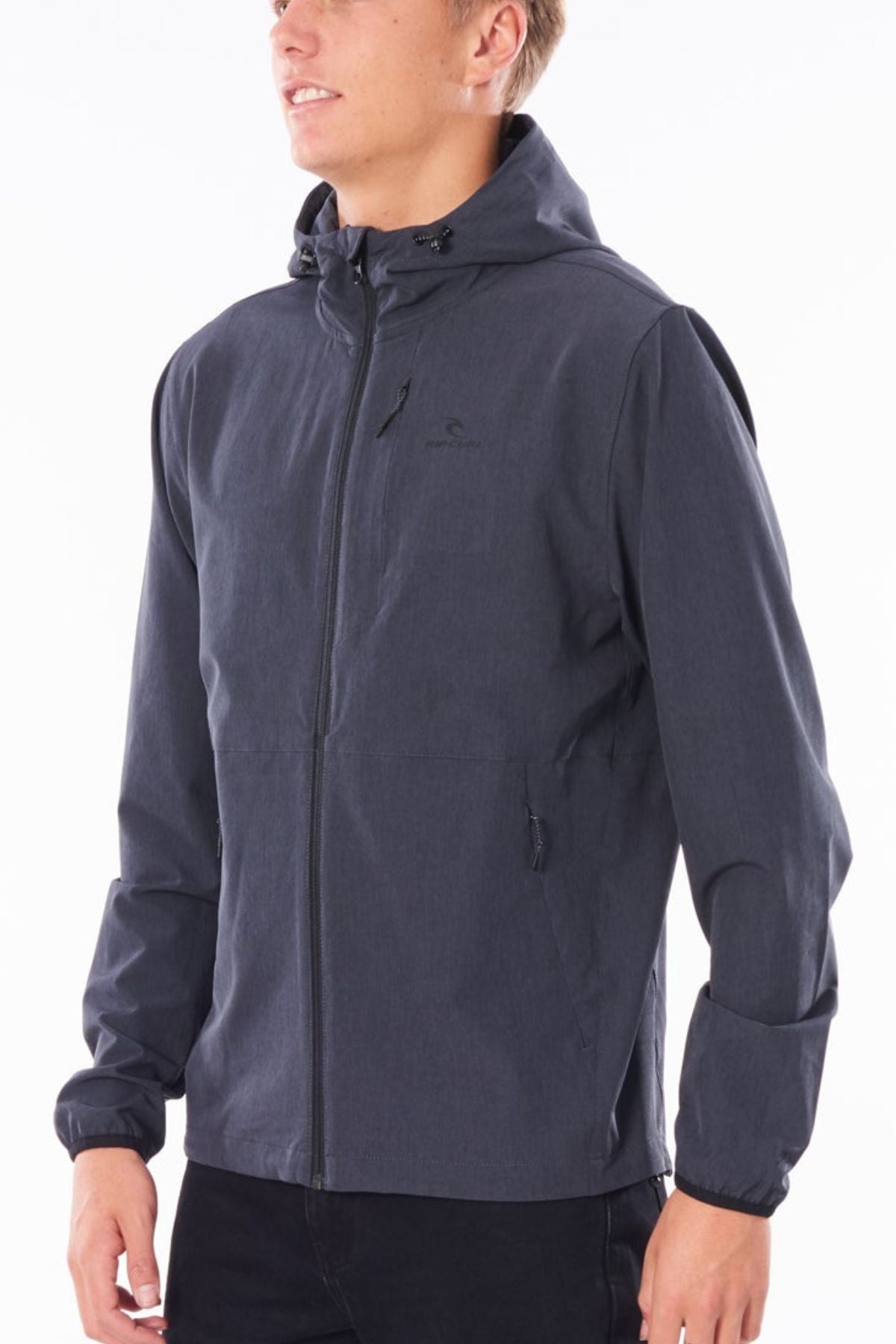 A person in the Rip Curl Anti Series Elite Jacket, a dark gray water-repellent jacket with front zipper and side pockets, stands against a plain white background with their face partially turned to the side and not fully visible.