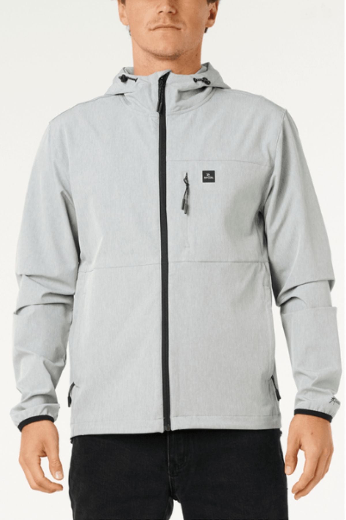 A man wears a Rip Curl Anti Series Elite Jacket in light gray—made from stretch polyester, featuring black zipper accents and a small chest pocket—standing against a plain background.