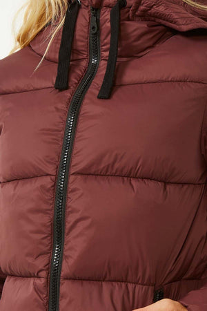 A close-up of a person donning the Rip Curl Anti Series Insulated Jacket in maroon. The jacket showcases a black zipper and hood drawstrings, with its quilted design enhanced by DWR water repellent treatment for optimal warmth. The individual’s hair is partially visible, cascading over the jacket.