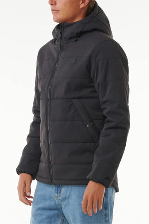 A man wearing the Rip Curl Anti Series Ridge Jacket, featuring quilted padded lining and a front zipper, pairs it with blue jeans while standing against a plain white background.