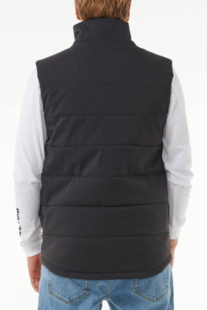 A person wearing the Rip Curl Anti Series Ridge Vest in black, featuring quilted padded lining, over a white long-sleeve shirt and blue jeans, shown from the back on a plain white background.