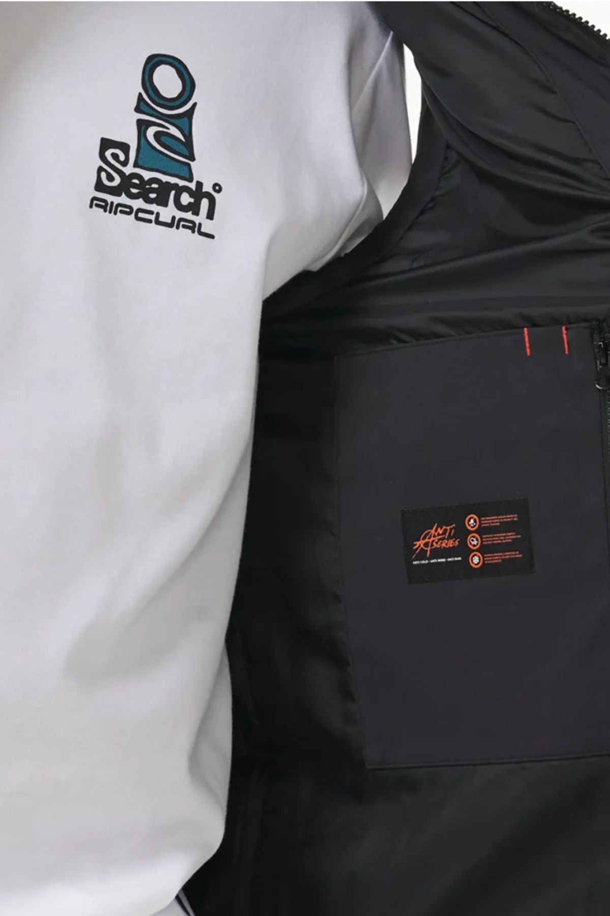 A person stands next to an open Rip Curl Anti Series Ridge Vest, revealing its quilted padded lining and a small interior label with orange text, while wearing a white Rip Curl shirt with a blue and black logo.