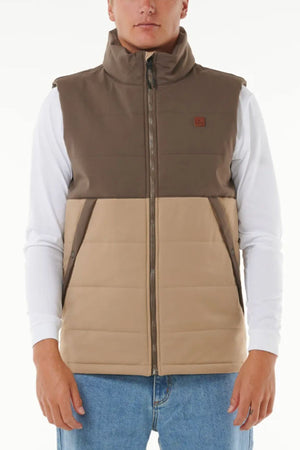 Wearing a Rip Curl Anti Series Ridge Vest with quilted padded lining and water repellent finish over a white long-sleeve shirt and blue jeans, this person stands against a plain white background.