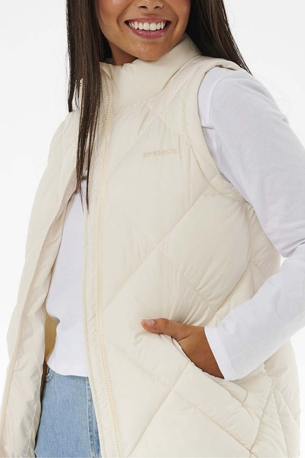 A smiling person is wearing a Rip Curl Anti Series Shorebreak Vest over a long-sleeved white shirt. They have one hand in their vest pocket and are standing against a plain background, ready for any outdoor adventure.