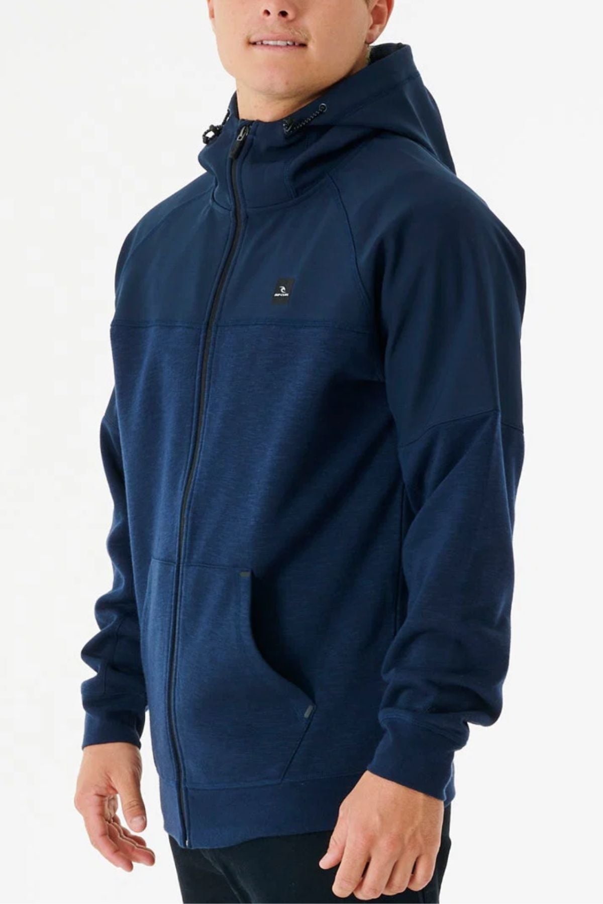A person wearing the Rip Curl Anti Series Viral Zip Thru, a dark blue, performance-driven jacket with a hood and front pockets, stands against a plain white background.