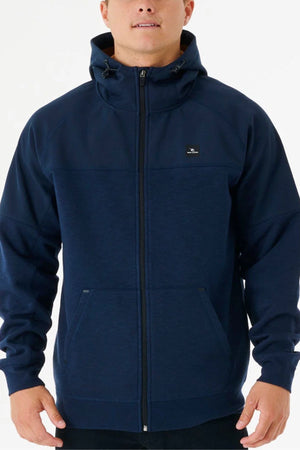 A person wearing the Rip Curl Anti Series Viral Zip Thru jacket in navy blue, featuring a hood, front pockets, and a small chest logo, stands against a plain white background. This jacket blends style with performance.