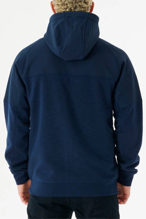 A person with short curly hair, wearing a dark blue Rip Curl Anti Series Viral Zip Thru jacket and black pants, is standing with their back to the camera against a plain white background.