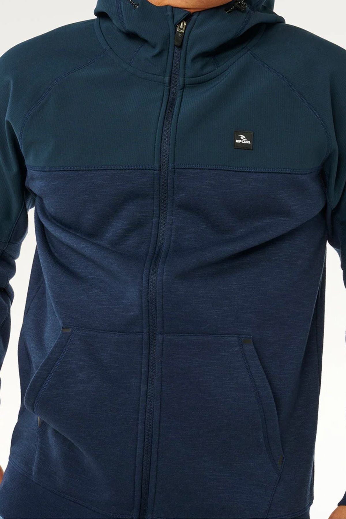 A person wearing a dark blue Rip Curl Anti Series Viral Zip Thru jacket with a small chest emblem and front pockets, shown from shoulders to hips.