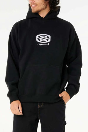 A person wears a black Rip Curl Archive Hood hoodie, featuring a white logo and front text, standing with one hand in the pocket against a plain background. Made from soft Cotton Poly Fleece for comfort.