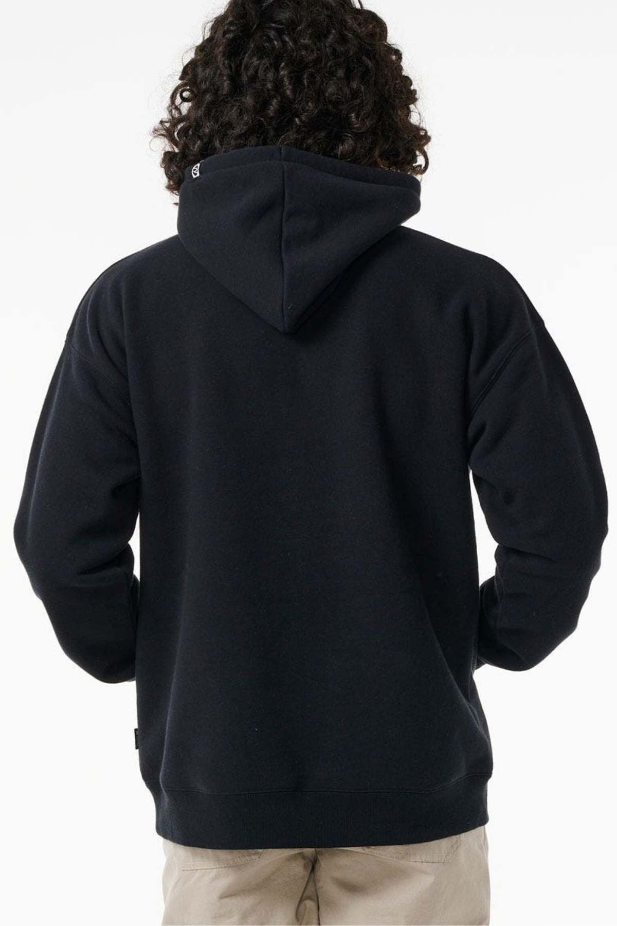 A person with curly hair is shown from the back, wearing a black Rip Curl Archive Ocean Tech Hood sweatshirt and beige pants, highlighting surf-inspired style against a plain white background.