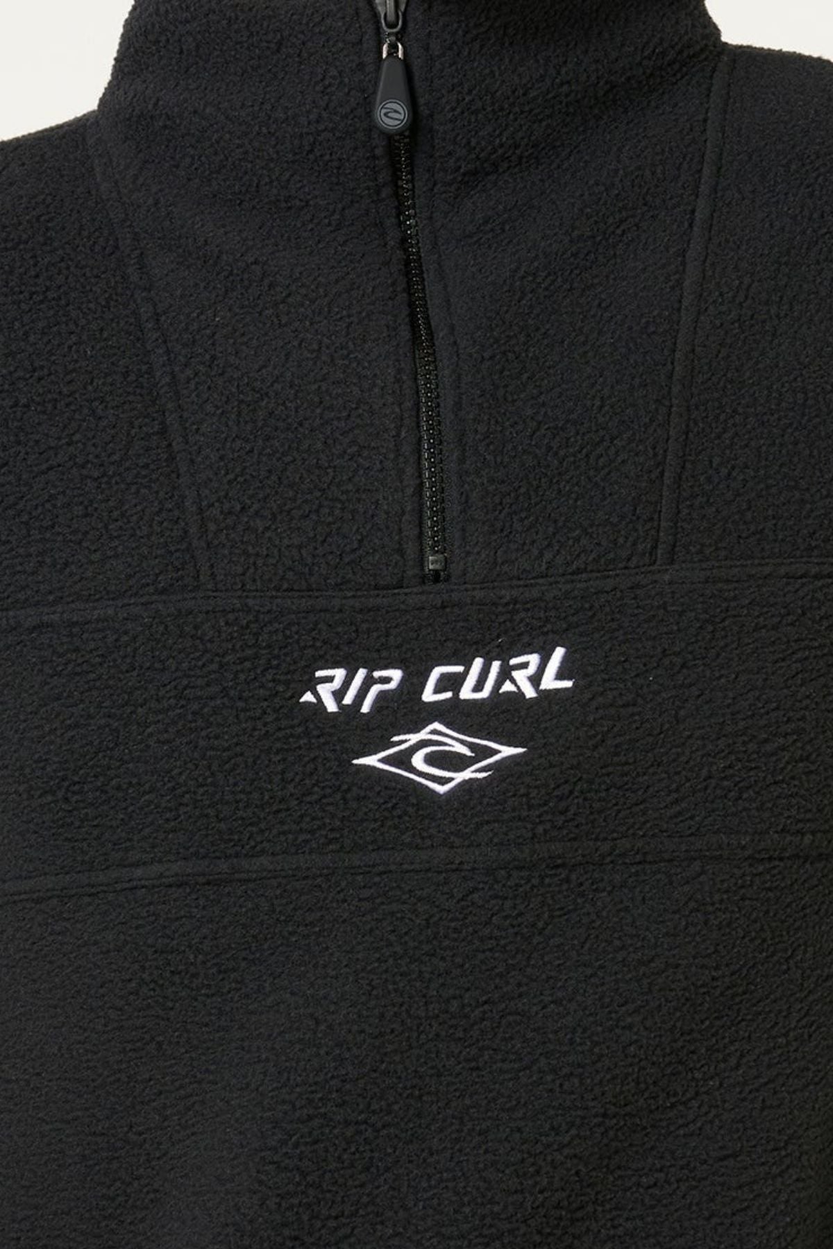 Close-up of the Rip Curl Bells Polar Fleece, showcasing its soft black fleece, half-zip design, zip pockets, and a white embroidered "RIP CURL" logo with wave on the chest.