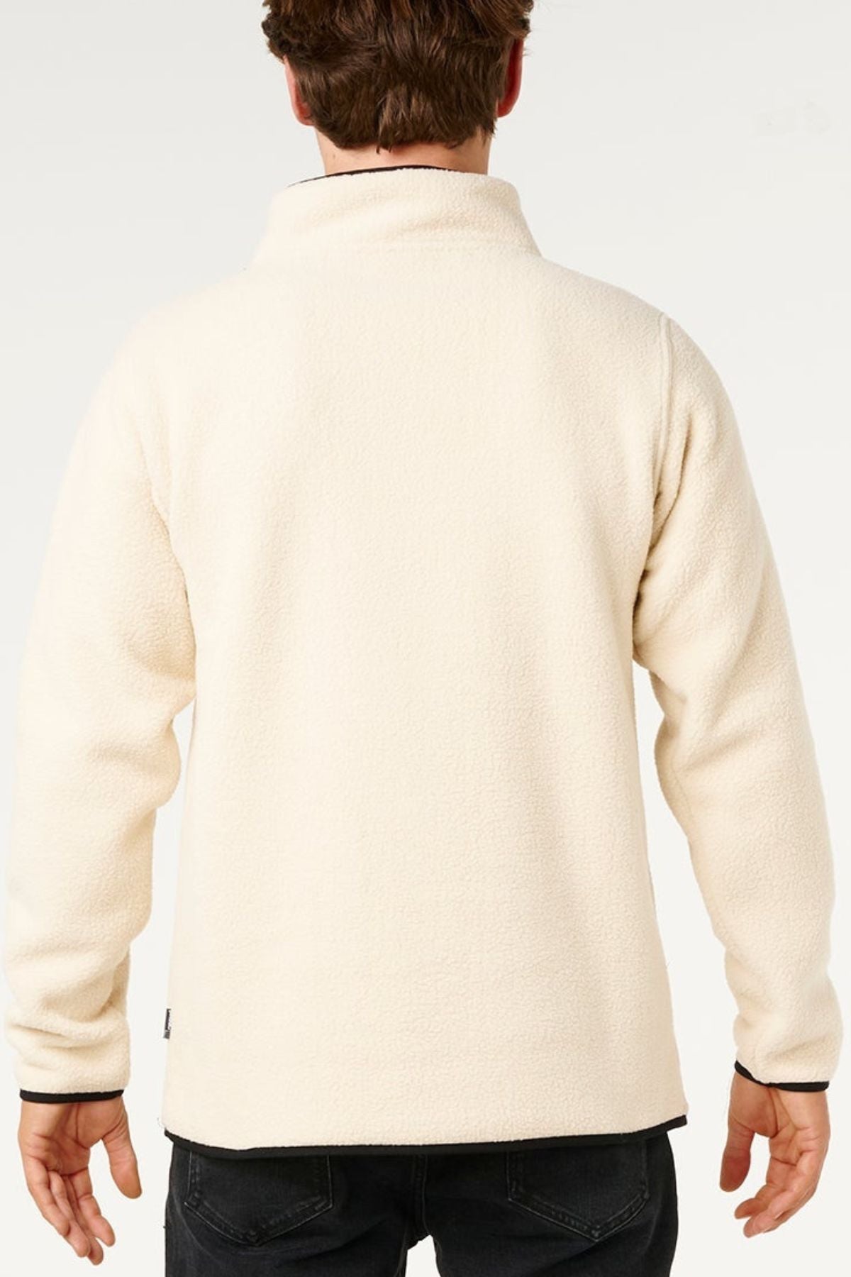 A person is seen from behind wearing the Rip Curl Bells Polar Fleece in cream with an embroidered chest logo and black pants, standing against a plain light background.