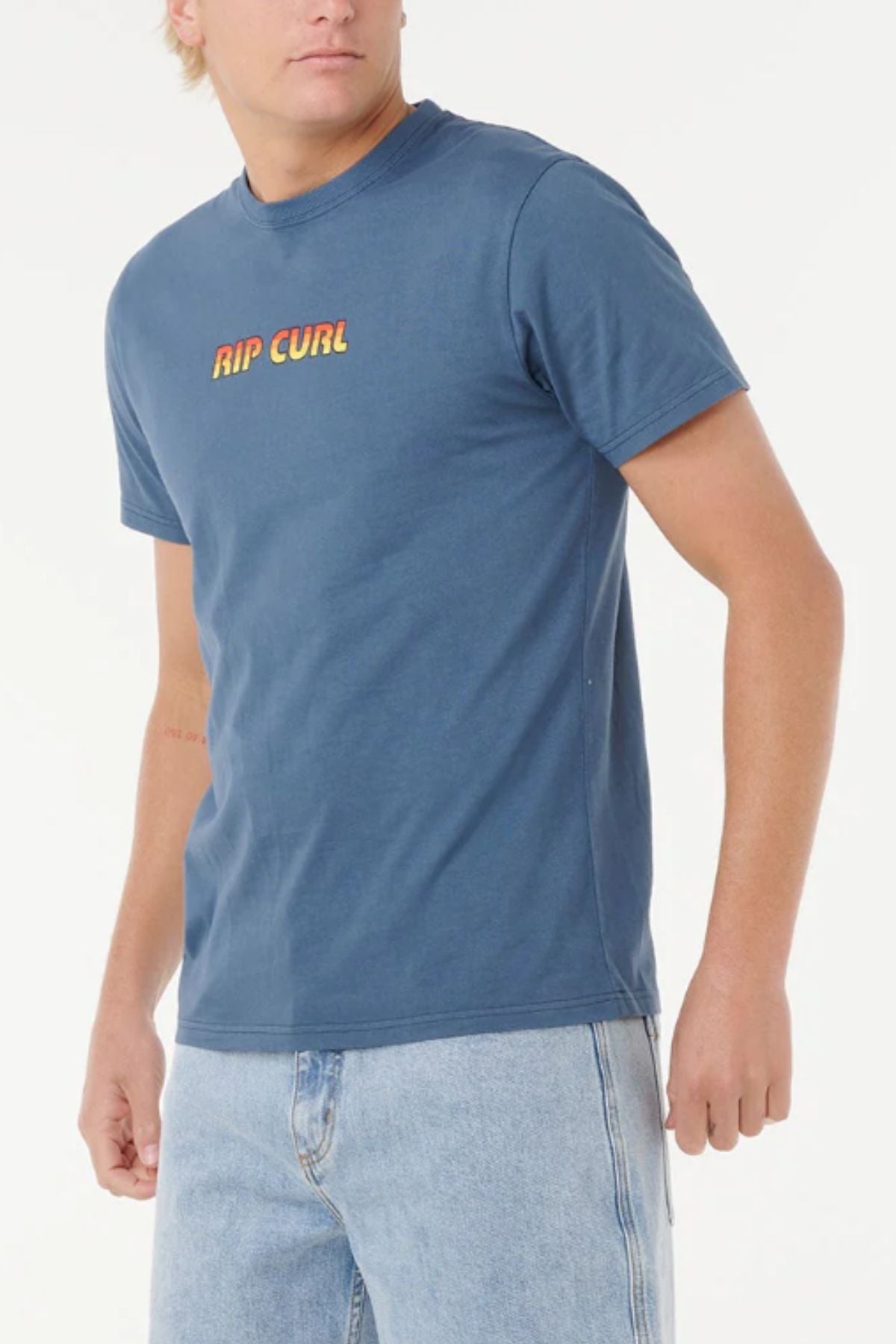 A person in a blue Rip Curl Big Mumma Icon Tee made from organic cotton and light blue jeans stands against a plain white background.