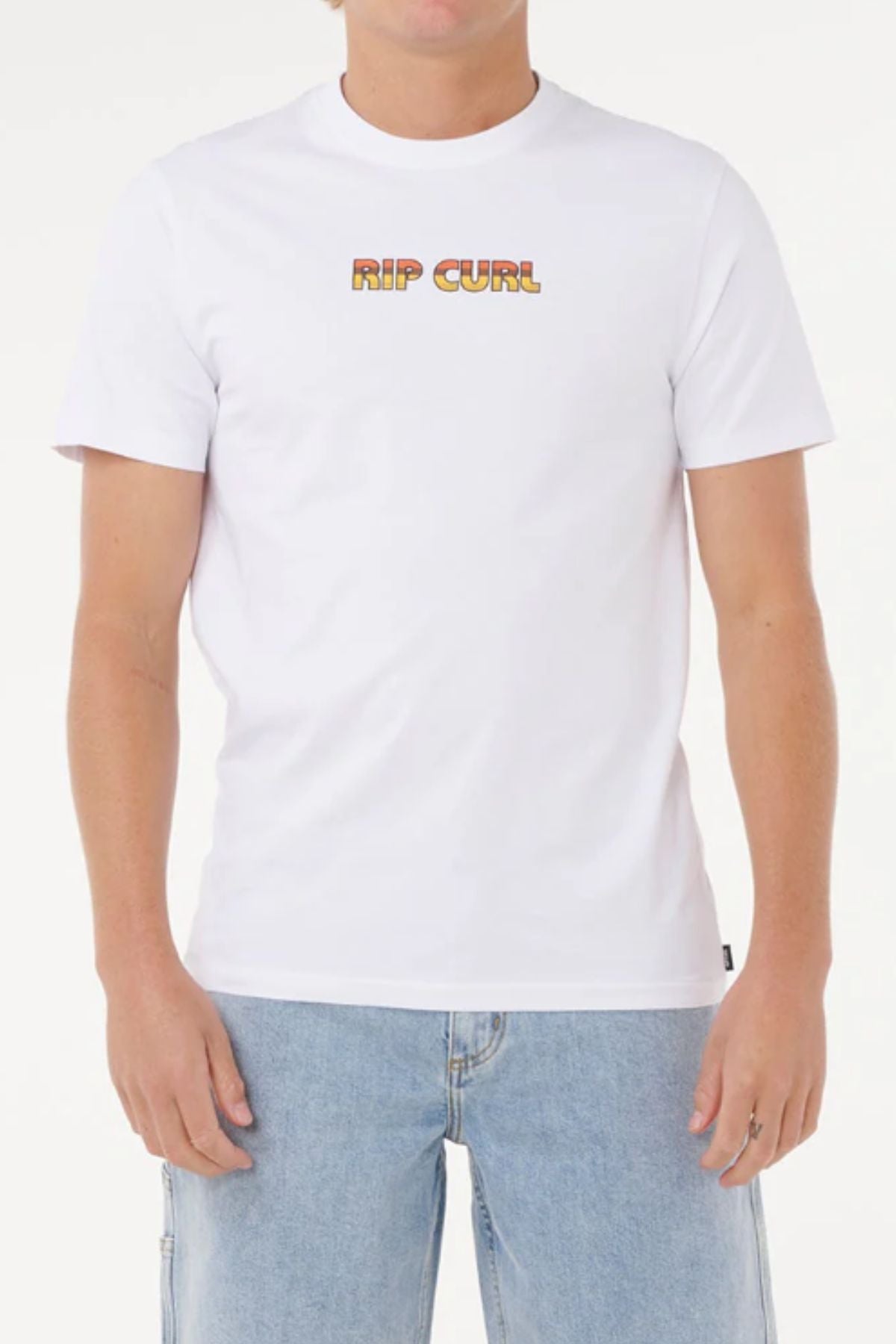 A person wearing the Rip Curl Big Mumma Icon Tee, made from organic cotton with orange-yellow gradient chest lettering, paired with light blue denim jeans against a white background.