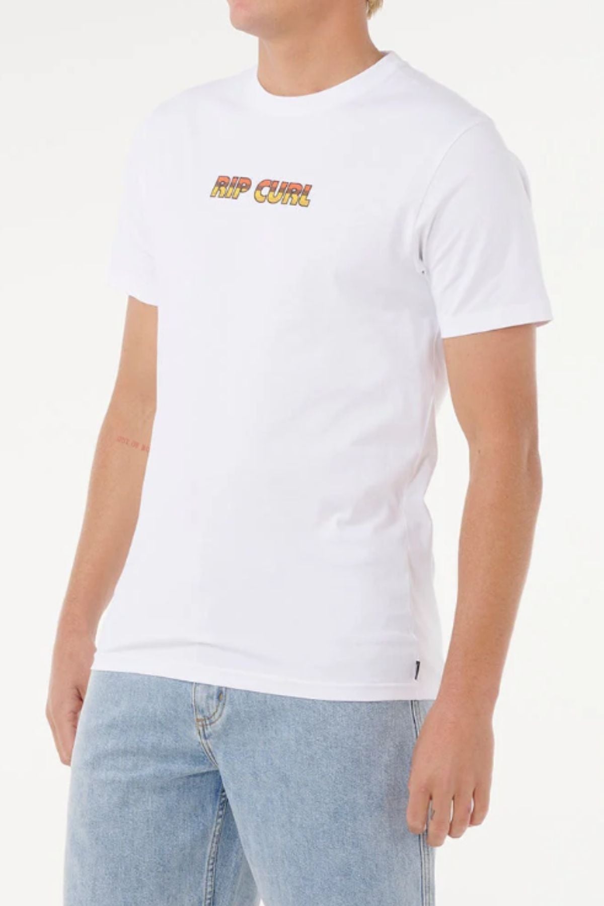 A person wears the Rip Curl Big Mumma Icon Tee, made from organic cotton and featuring colorful chest lettering, paired with light blue jeans. The casual look stands out on a white background, with the face partially out of view.