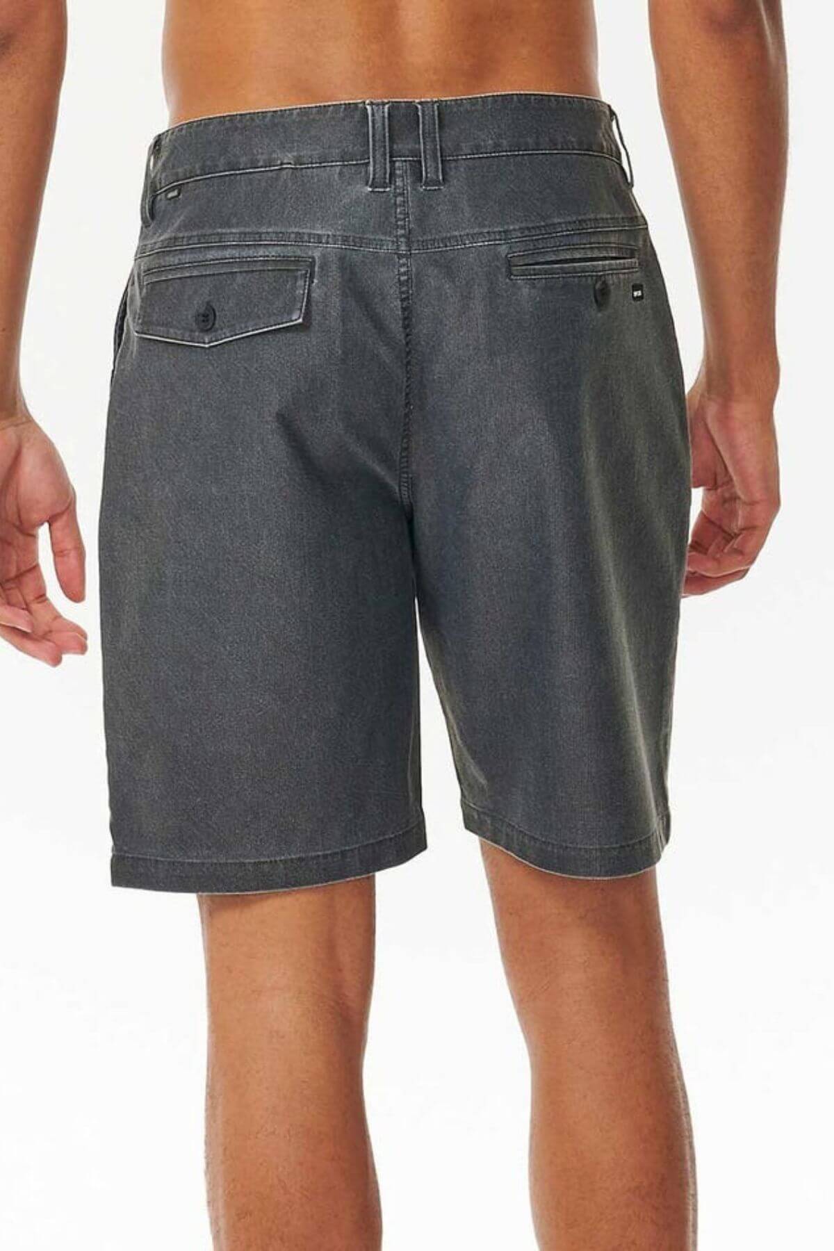 A person stands with their back to the camera, highlighting Rip Curl Boardwalk Epic Mix shorts in dark gray. These shorts feature belt loops, multiple pockets, and a vintage-inspired look. Made from quick-dry fabric, they're perfect for adventures against the plain light background.