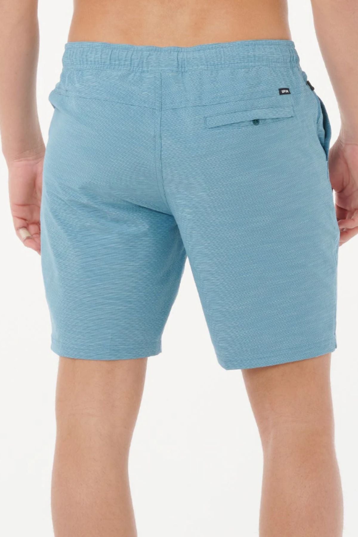 A person is shown from the waist down, wearing light blue Rip Curl Boardwalk Jackson Volley water-repellent shorts with a back pocket and elastic waistband, standing against a plain white background.