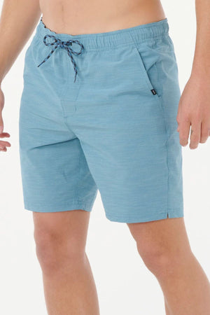 A person wearing light blue Rip Curl Boardwalk Jackson Volley shorts stands against a plain white background, with hands relaxed at their sides. Only the lower torso and upper legs are visible.