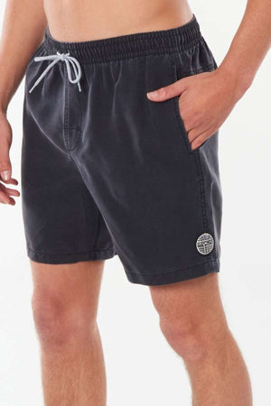 The individual is sporting the Rip Curl Bondi Volley shorts in dark gray, which have a circular logo on the left leg. Crafted from recycled PET, these board shorts include side pockets, and they are posed with one hand in a pocket to showcase both front and side views.