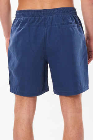 The image displays an individual from the waist down wearing blue Rip Curl Bondi Volley shorts, which include a back pocket. Crafted from recycled polyester ripsuede and equipped with quick-dry technology, these shorts are highlighted for their comfort and style against the simple backdrop.