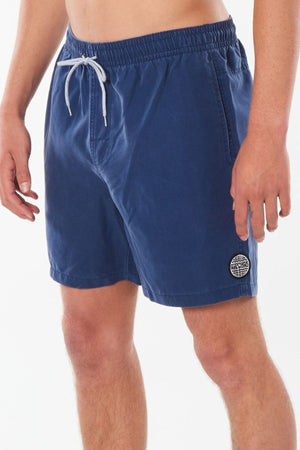 Someone wearing Rip Curl Bondi Volley swim shorts crafted from recycled Polyester Ripsuede with quick dry technology. These blue shorts include a gray drawstring and feature a circular logo on the left side near the hem, set against a plain white background.