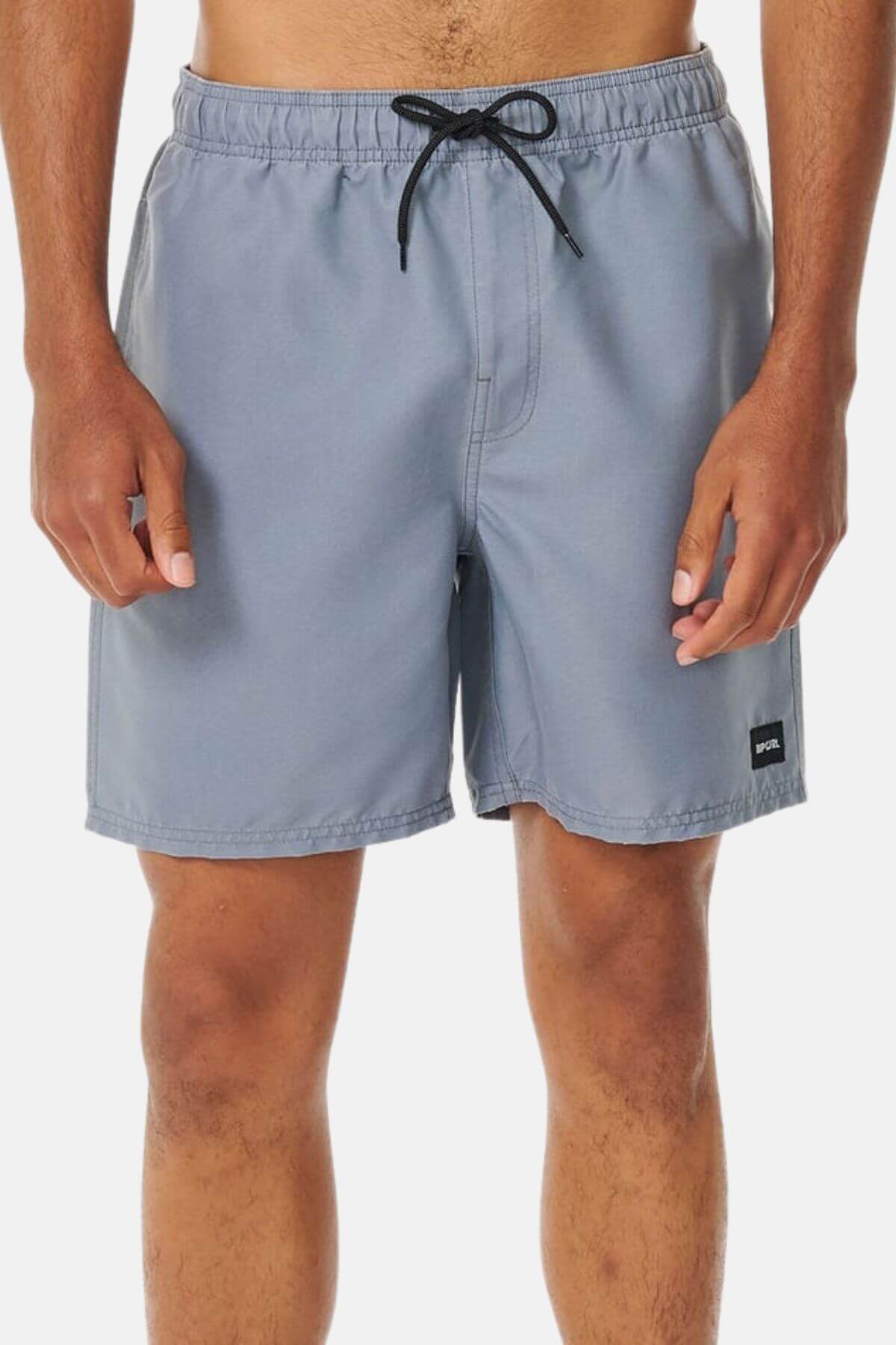 Someone is wearing light gray Rip Curl Bondi Volley shorts, made from recycled PET with a black logo patch on the left leg, standing in front of a plain white background.
