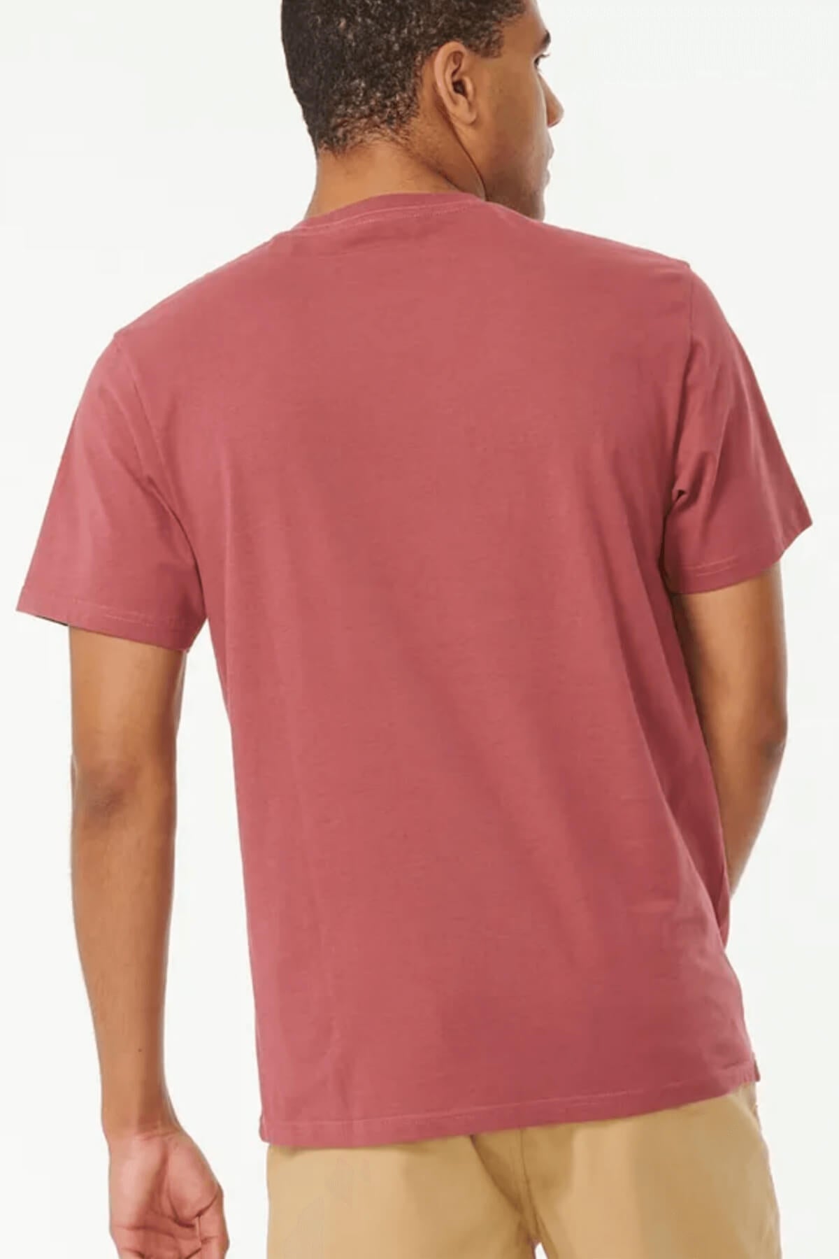 A person with short hair stands with their back to the camera, wearing a red Rip Curl Brand Icon Tee and beige pants. This classic crew neck T-shirt is made from 100% cotton and set against a plain white background.